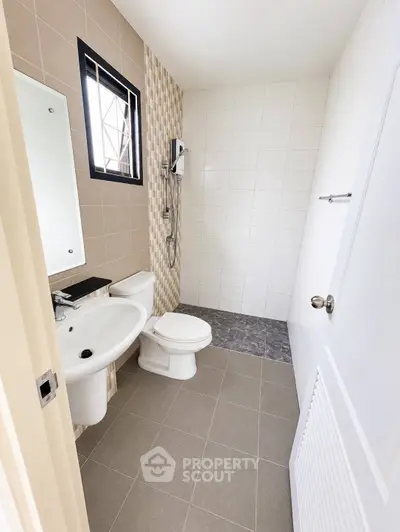 Modern bathroom with sleek fixtures and neutral tiles, featuring a shower and a large window for natural light.