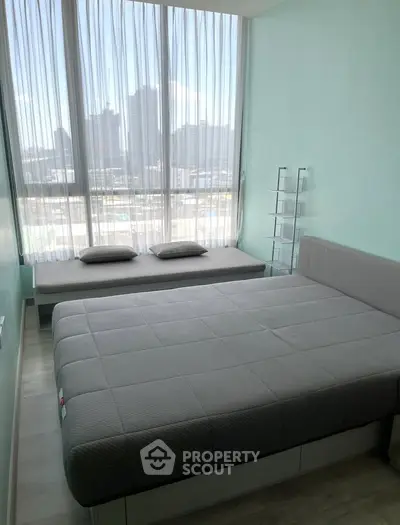 Modern bedroom with large windows and city view, featuring stylish gray bedding and minimalist decor.