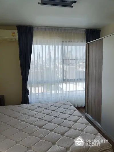 Bright bedroom with large window and city view, featuring modern wardrobe and air conditioning.