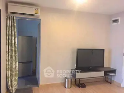 Modern living room with TV and air conditioning, adjacent to a kitchen with a fridge.