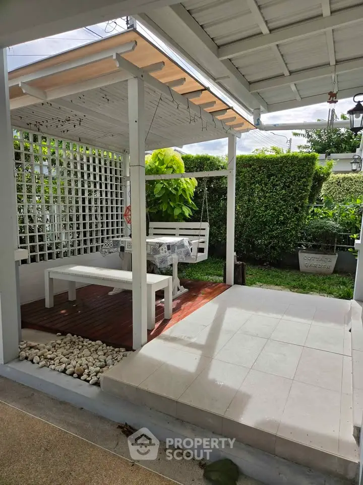 Charming outdoor patio with white pergola and lush greenery, perfect for relaxation and entertaining.