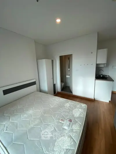 Modern bedroom with compact kitchen and minimalist design, featuring a cozy bed and sleek wooden flooring.