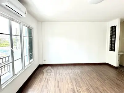 Spacious empty room with wooden flooring and large windows in a modern apartment.