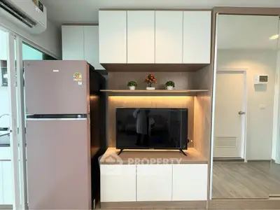 Modern living room with sleek cabinetry and mounted TV, featuring a stylish refrigerator and elegant decor.