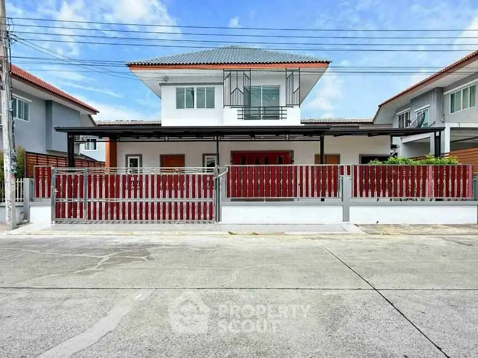 Modern two-story house with red fence and spacious driveway in suburban neighborhood.