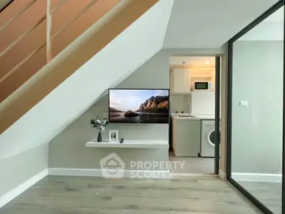Modern living space with TV under stairs, washing machine, and microwave in compact layout.