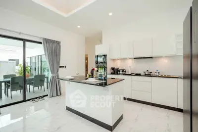 Modern kitchen with island and open layout, featuring sleek white cabinetry and marble flooring.