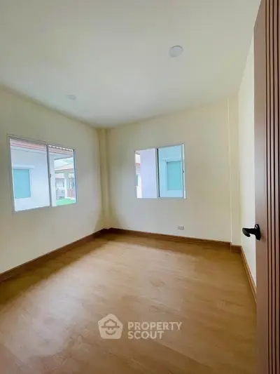 Spacious empty room with wooden flooring and large windows in a modern home.