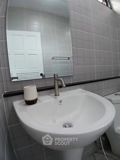 Modern bathroom with sleek sink and mirror in stylish tiled setting.