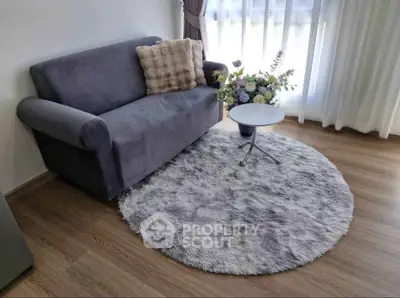 Cozy living room with plush gray sofa, round rug, and elegant floral arrangement by window.