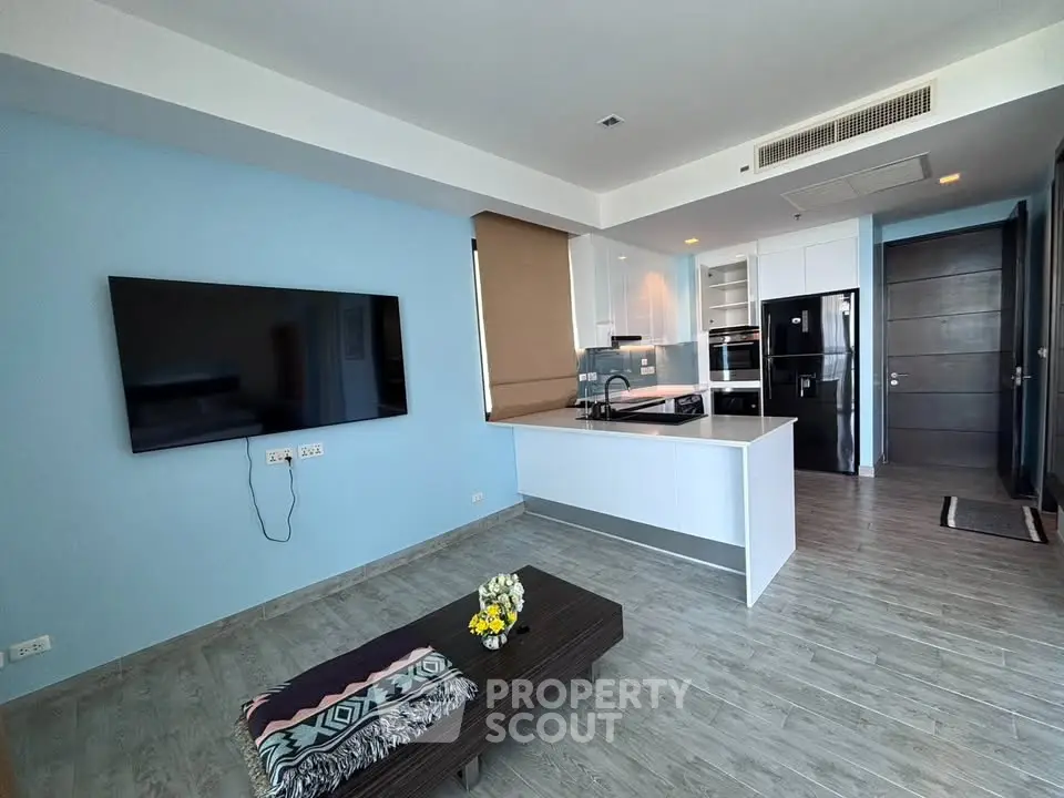 Modern open-layout living room with sleek kitchen and large wall-mounted TV
