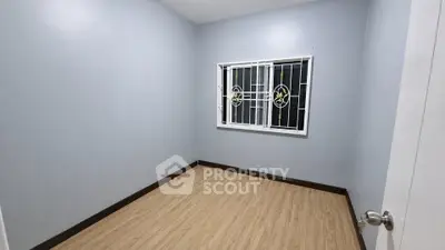 Spacious empty room with wooden flooring and decorative window grille, perfect for customization.