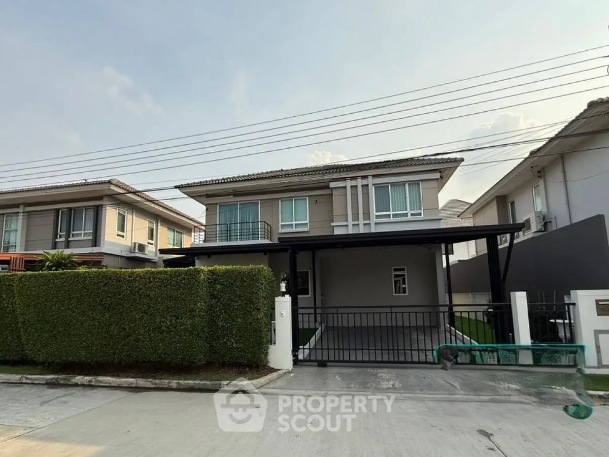 Modern two-story house with manicured hedge and gated driveway in suburban neighborhood.