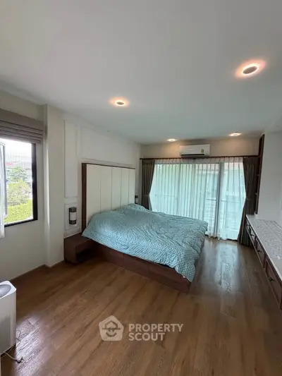 Spacious bedroom with large windows and modern decor, featuring a comfortable bed and wooden flooring.