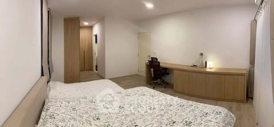 Spacious bedroom with modern decor and study area, featuring a comfortable bed and sleek wooden furniture.