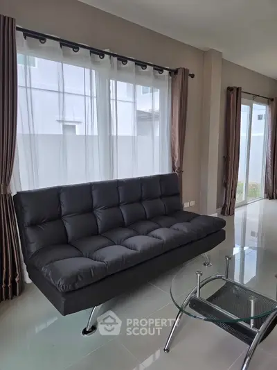 Modern living room with sleek black sofa and glass coffee table, bright natural light through large windows.