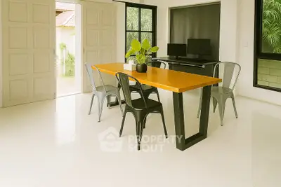 Modern dining area with sleek table and chairs, featuring large windows and lush greenery view.