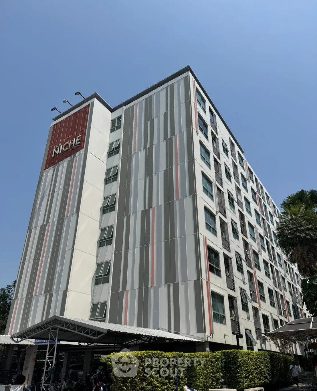 Modern multi-story building with unique facade design and lush greenery.