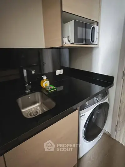 Modern compact kitchen with sleek black countertops, built-in microwave, and washing machine.