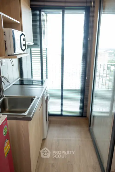 Modern compact kitchen with balcony view, featuring sleek appliances and wooden cabinetry.