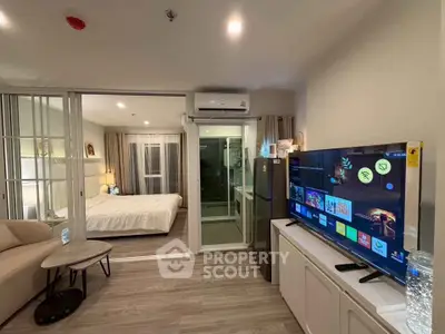 Modern open-plan living room with TV and bedroom view, featuring sleek design and natural light.