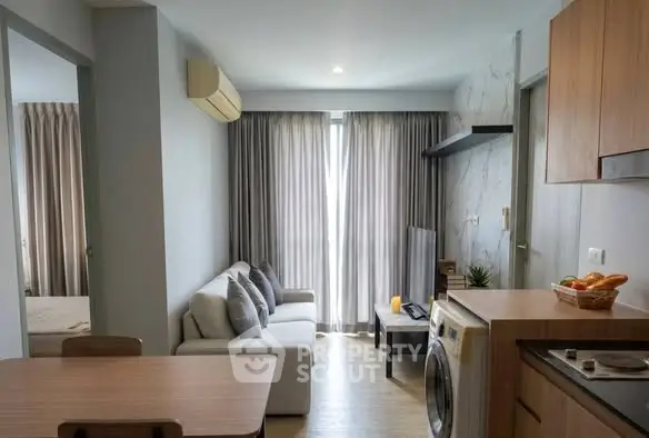 Modern living room with open kitchen and washing machine, featuring cozy sofa and natural light.