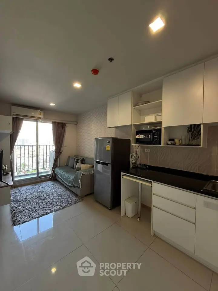 Modern open-layout living room with kitchen, featuring sleek appliances and balcony access.