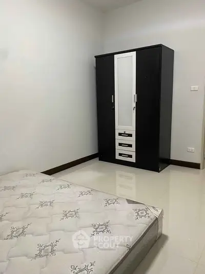 Minimalist bedroom with sleek wardrobe and mattress on polished floor.