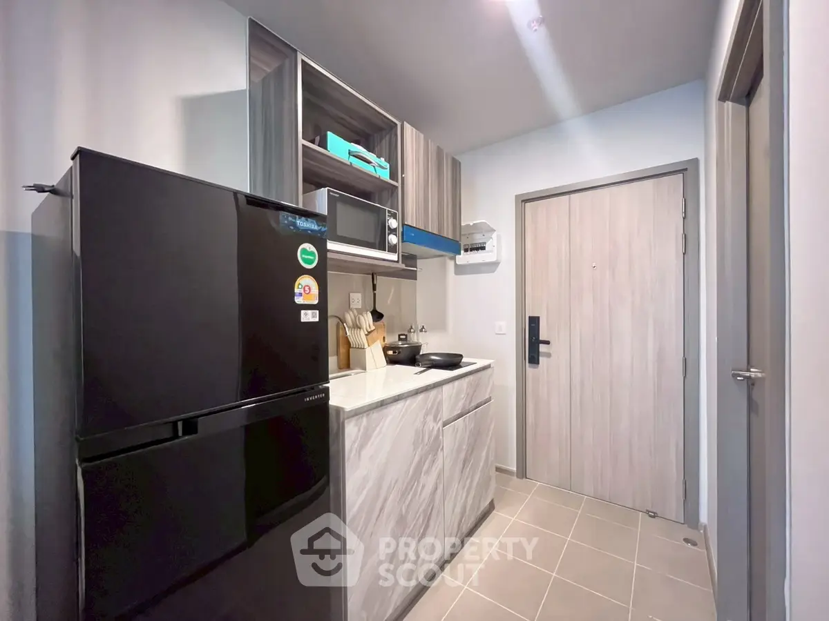 Modern compact kitchen with sleek black fridge and microwave, stylish cabinetry, and elegant tile flooring.