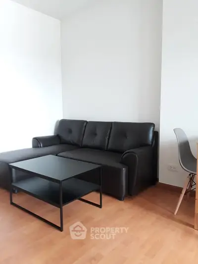Modern living room with sleek black sofa and minimalist coffee table on wooden flooring.