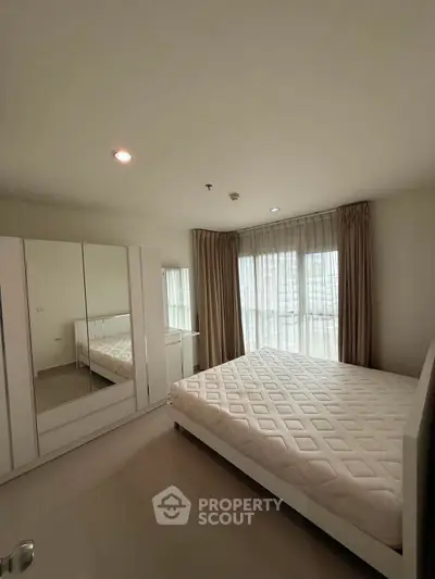 Spacious bedroom with large windows and modern furnishings in a bright apartment.