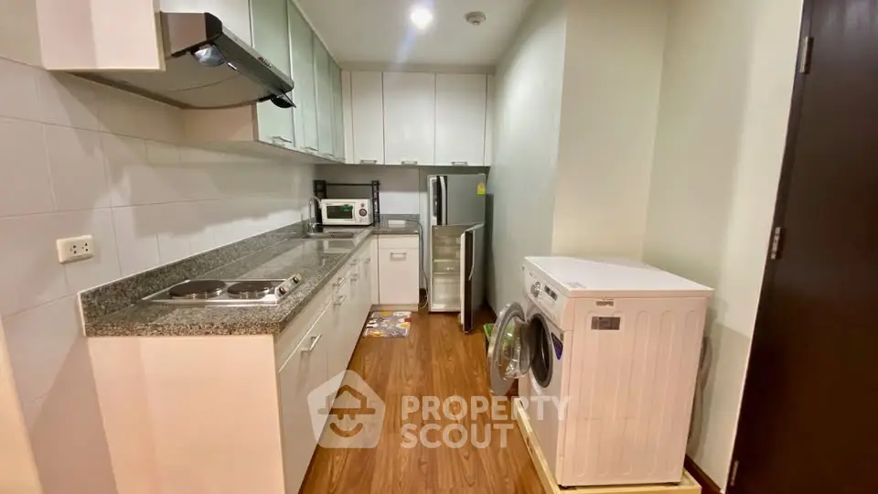 Modern kitchen with sleek appliances and wooden flooring, featuring a washing machine and ample storage.