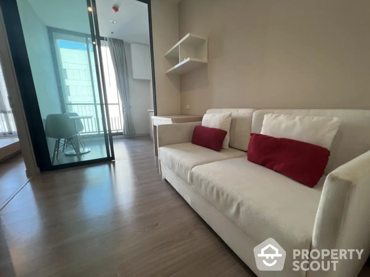 Modern living room with sleek design and glass partition leading to a bright balcony.