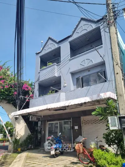 Charming three-story building with balconies and lush greenery in urban setting.