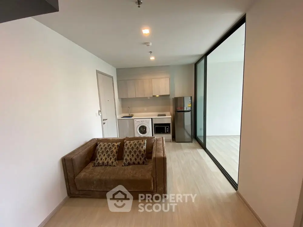 Modern living room with compact kitchen and washing machine in open layout apartment.