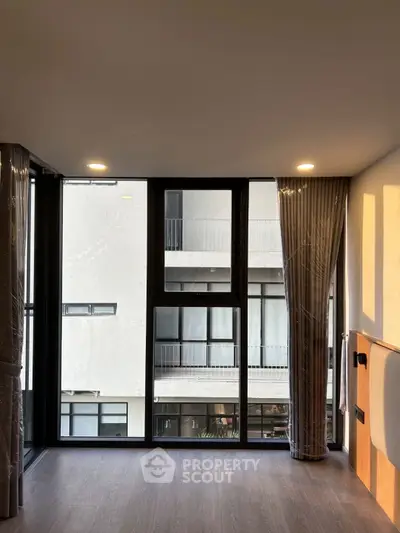 Modern apartment interior with large windows and city view, featuring sleek flooring and stylish curtains.