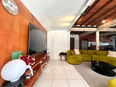 Stylish living room with modern decor and open kitchen layout, featuring unique green sofas and wooden accents.