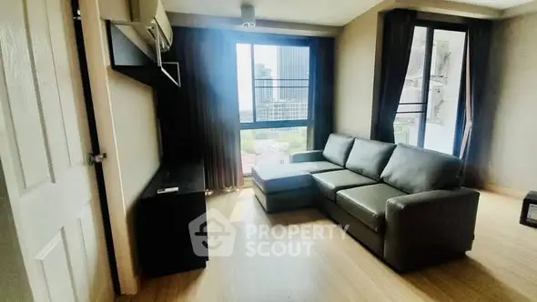 Modern living room with large windows and city view, featuring a sleek gray sofa and wooden flooring.