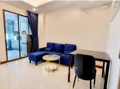 Modern living room with blue sofa, sleek table, and glass door leading to kitchen.