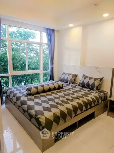 Modern bedroom with large window and stylish decor, offering a serene view of lush greenery.