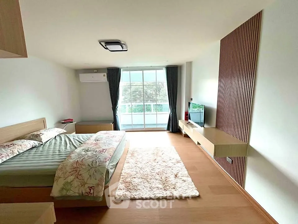 Spacious bedroom with modern decor and large window offering natural light.
