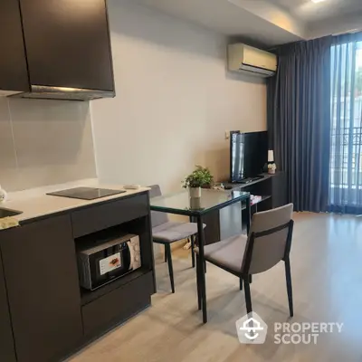 Modern living room with sleek kitchen and dining area, featuring stylish furniture and natural light.