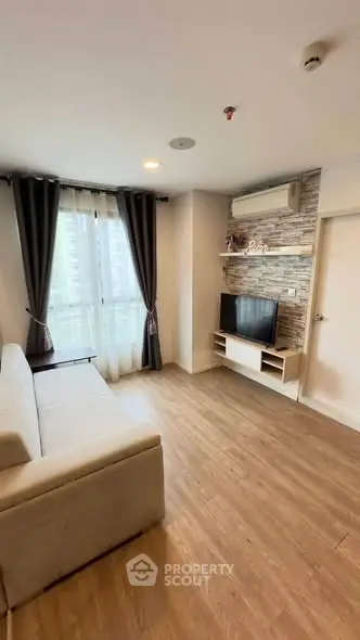 Modern living room with wooden flooring, cozy sofa, and wall-mounted TV in a bright apartment.