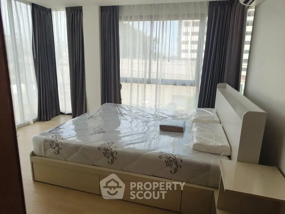 Spacious bedroom with large windows and modern furnishings in a high-rise apartment.