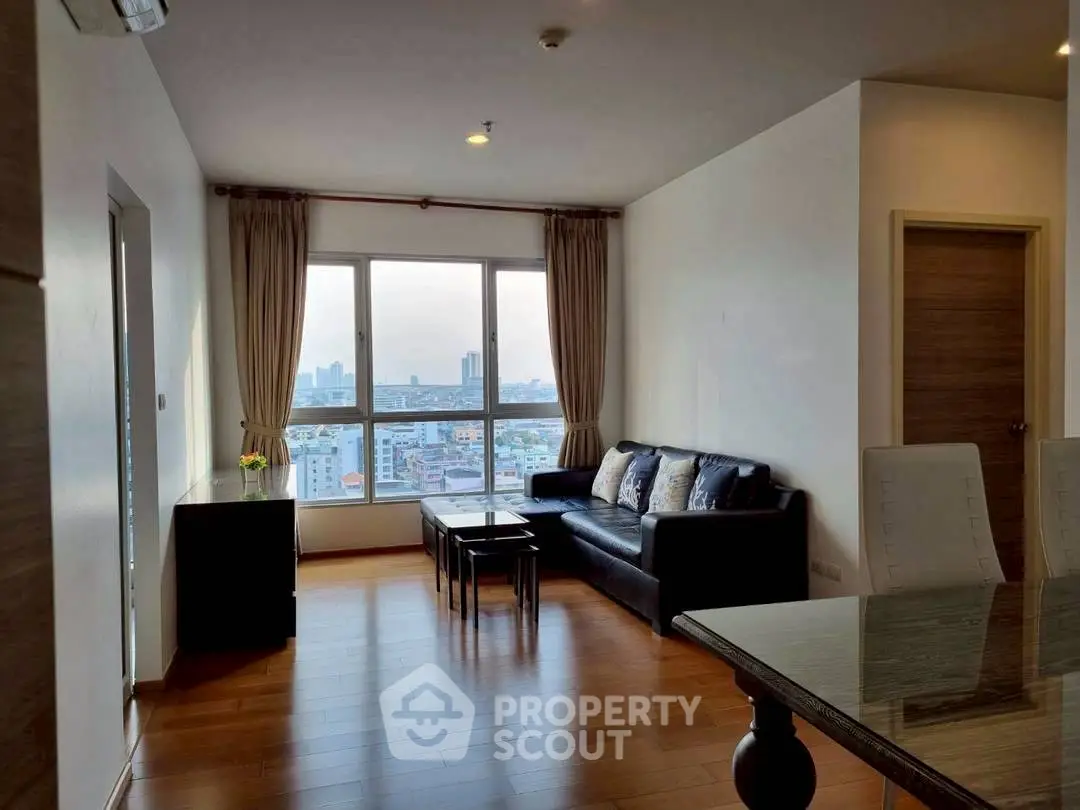 Spacious living room with city view, wooden flooring, and modern furniture in a high-rise apartment.