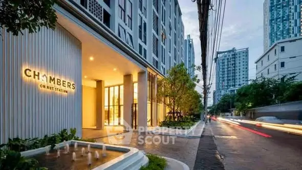 Modern apartment building entrance with illuminated signage and street view.