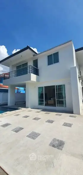 Modern two-story house with spacious balcony and large windows under clear blue sky.