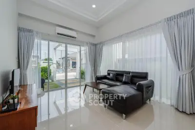 Modern living room with sleek black leather sofa and large windows offering natural light and garden view.