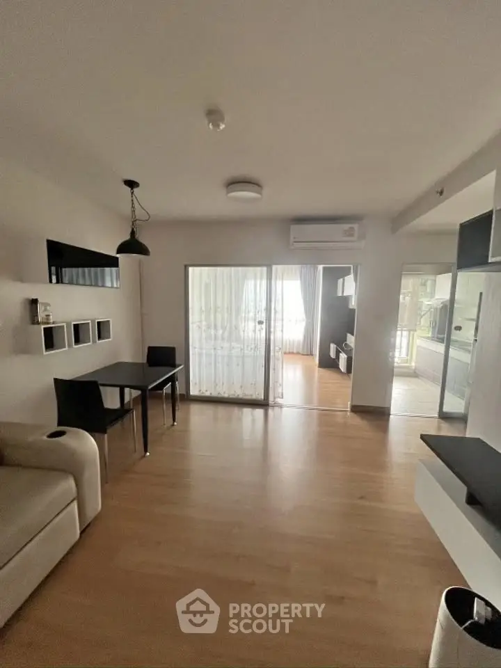 Spacious modern living room with wooden flooring and large windows leading to a balcony.
