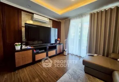 Spacious living room with modern decor and large TV, featuring elegant curtains and wooden flooring.